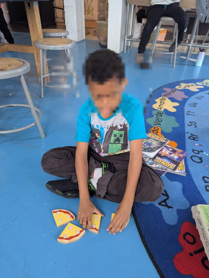 A child sitting on a blue rug working with fraction pieces that resemble pizza slices