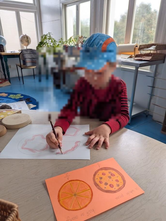A child wearing a cap drawing pizza shapes on paper at a desk, with an orange worksheet showing fraction drawings visible