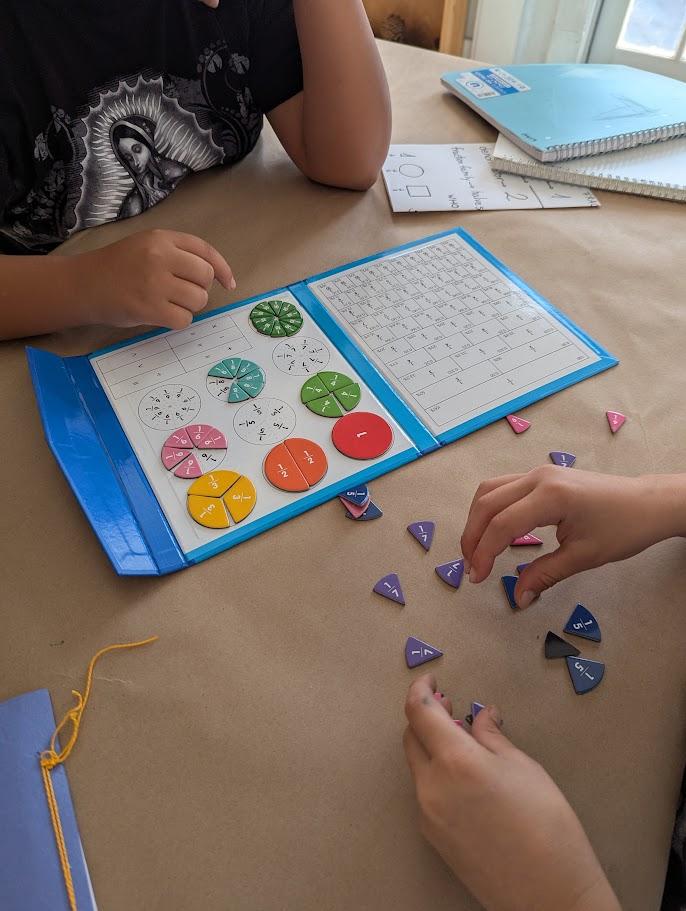 Two children's hands working with colorful fraction circle pieces and a fraction chart, sorting purple triangular fraction tiles