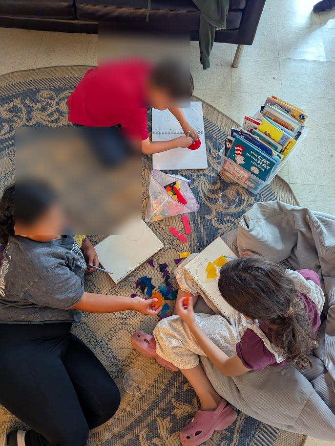 Three children working on the floor with books and materials, seen from above