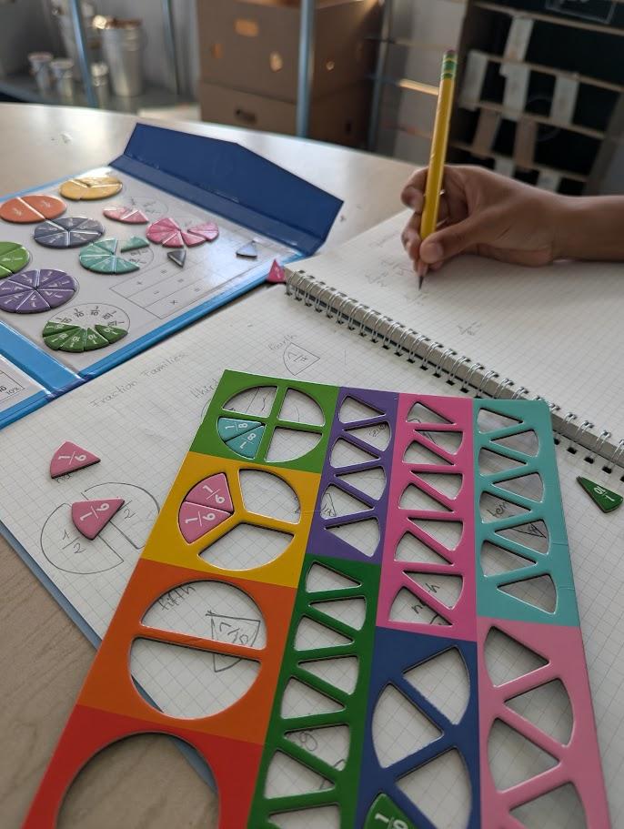 Colorful fraction pieces and manipulatives with a child writing in a notebook
