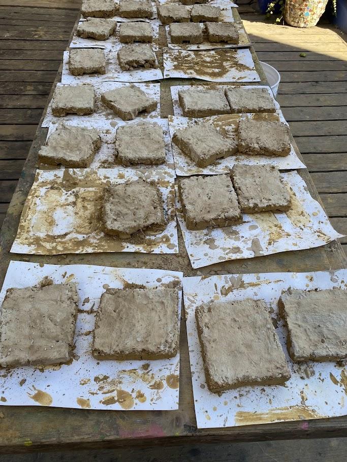Rows of adobe tiles drying in the sun — square and rectangular clay tiles laid out flat on a surface