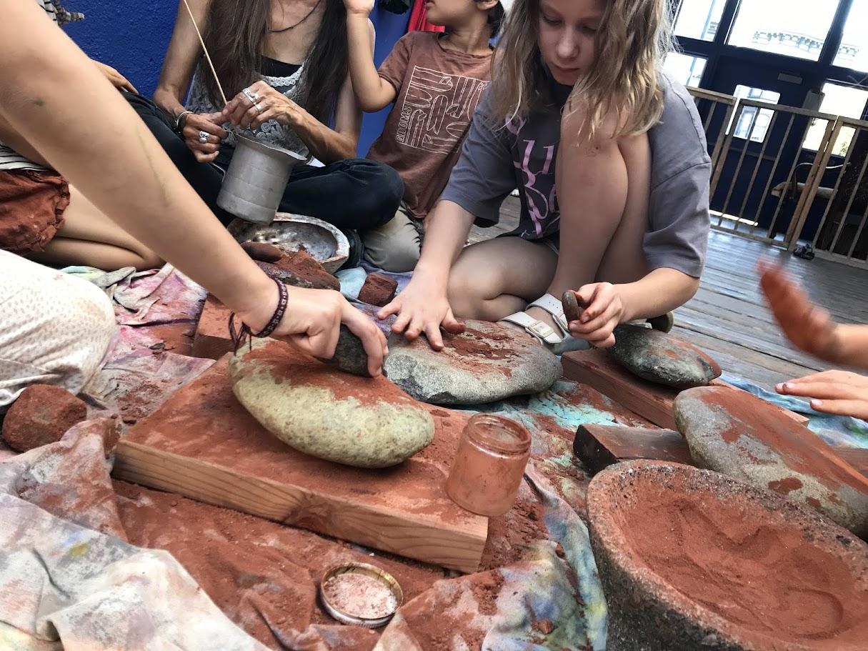 Children's hands working with clay and adobe mixture on a table — multiple hands pressing and shaping the earth material