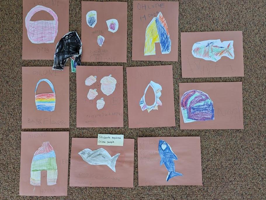 Children's drawings on pink paper spread on the floor — fish, shells, baskets, and animals drawn after researching Ohlone books
